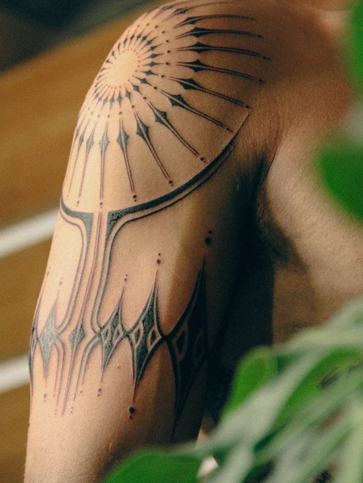 Geometric black ink tattoo on a man's shoulder and upper arm with sunburst patterns.