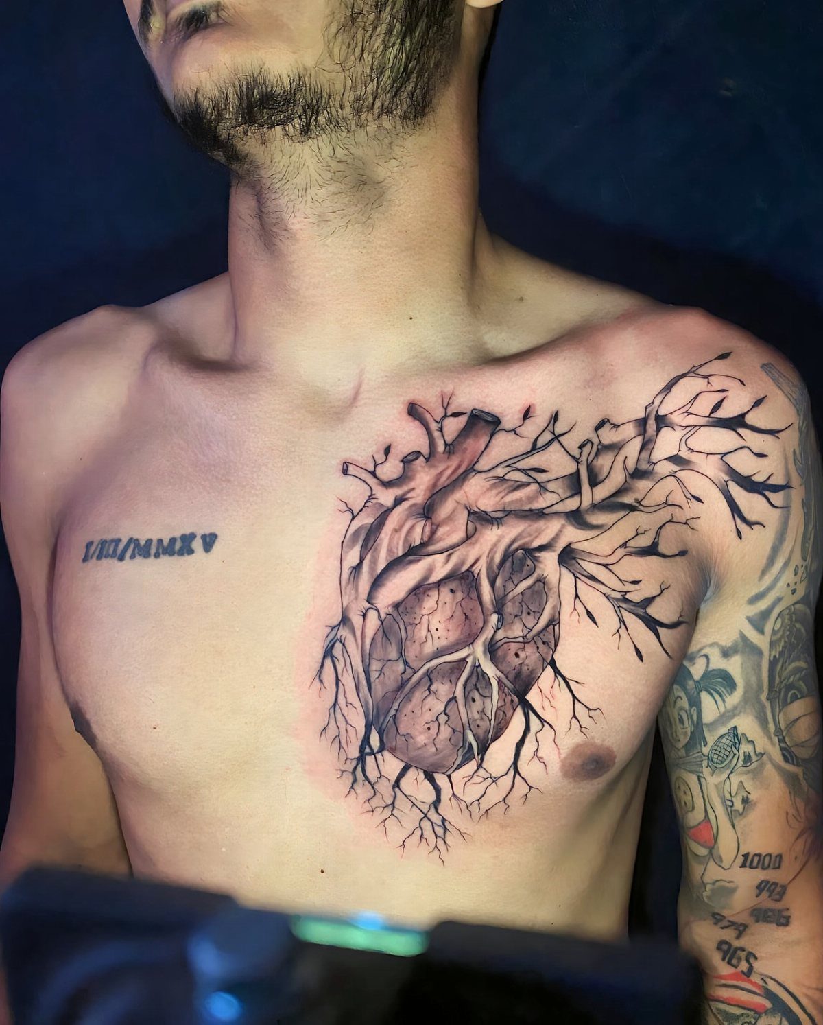 Anatomical heart tattoo on a man's chest with detailed black ink branching veins.