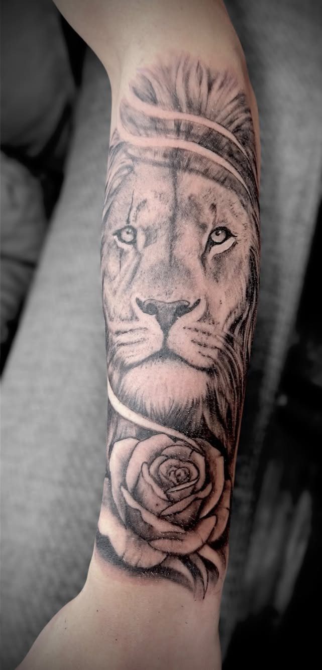 Lion face tattoo with a rose on a person's forearm in black ink.