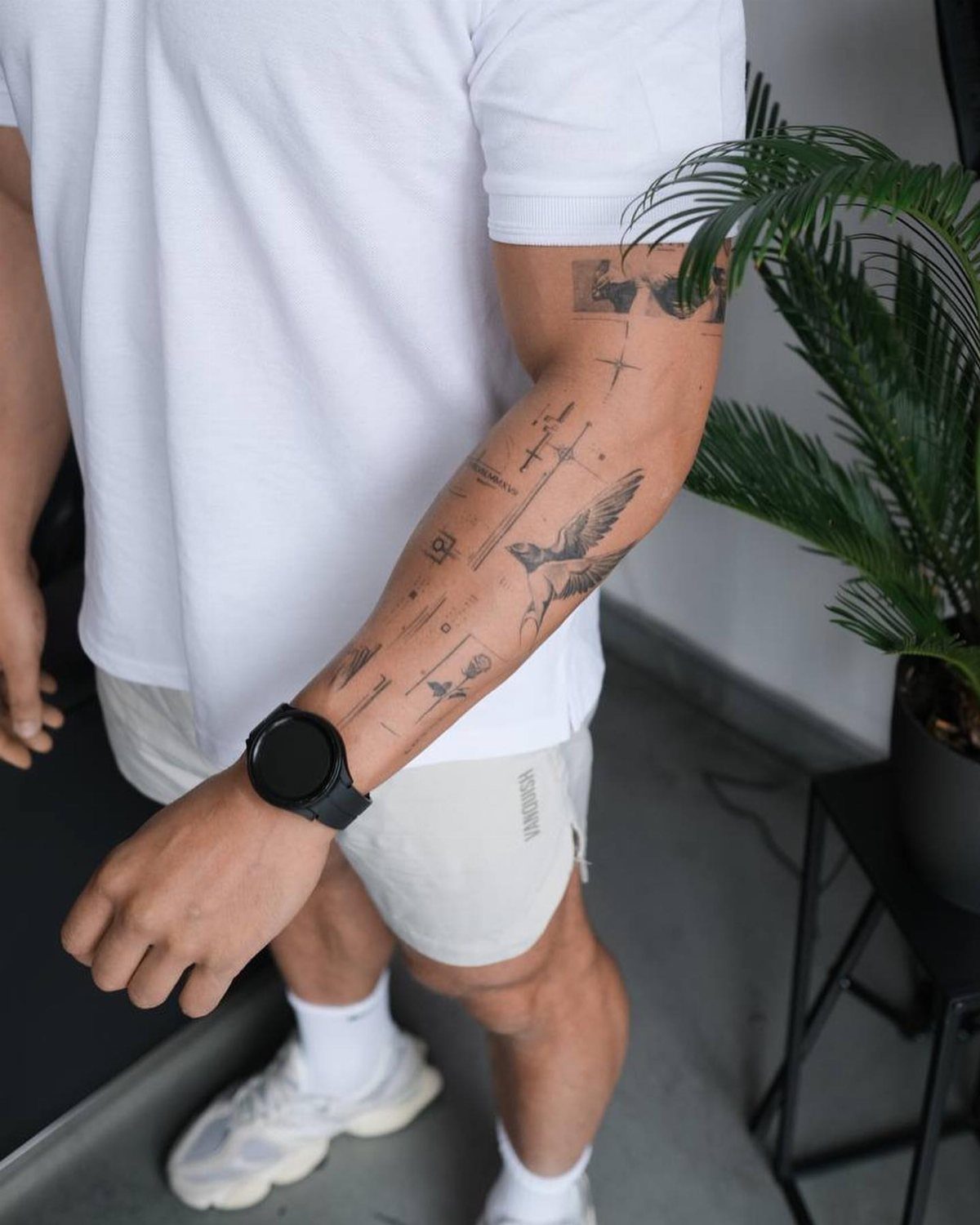 Man's forearm featuring several small, clean black ink minimalist tattoos including a bird.