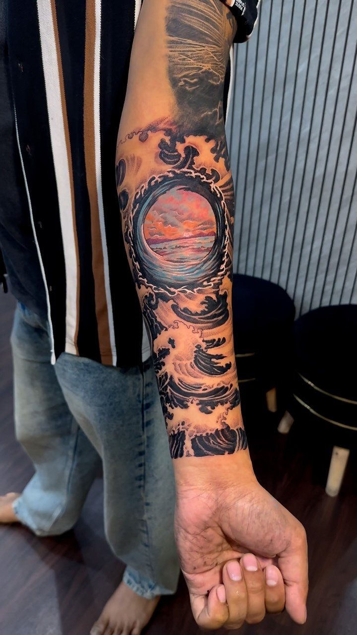Forearm tattoo of crashing ocean waves encircling a circular sunset sea scene.