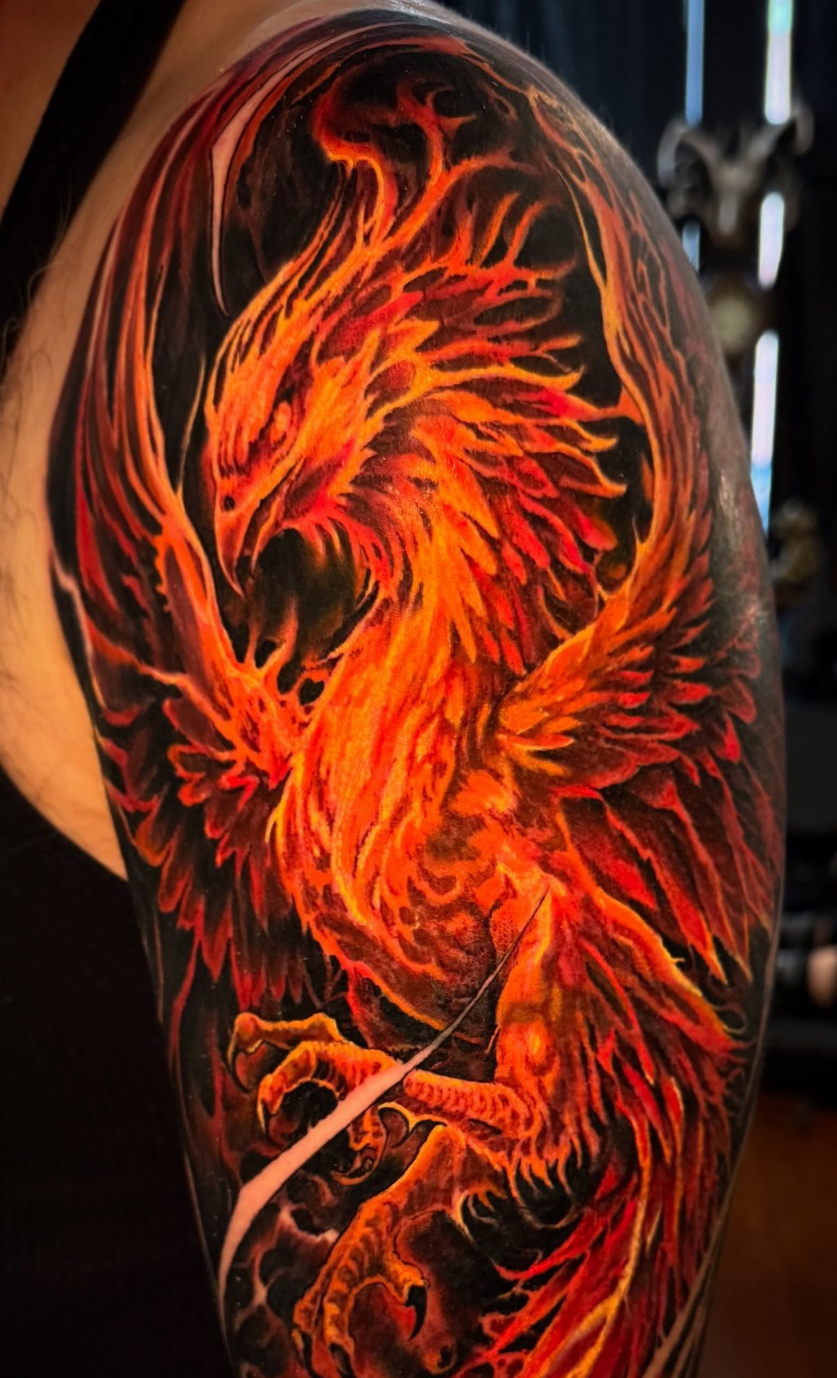Fiery orange and red phoenix tattoo on a man's upper arm with black shading.