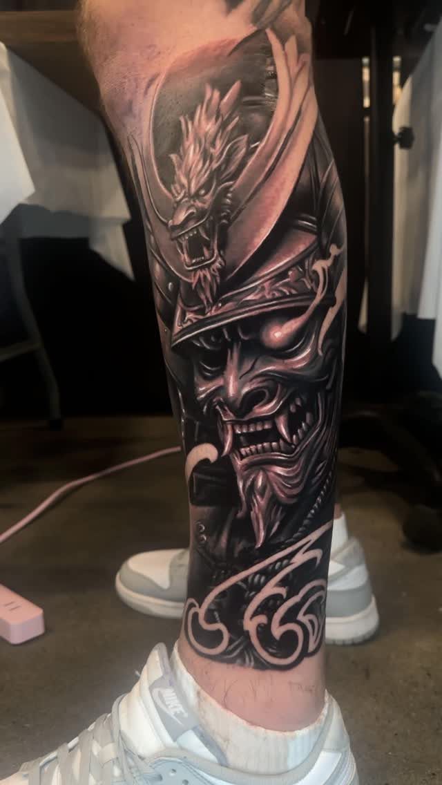 Samurai tattoo on a lower leg featuring a demonic mask and dragon helmet.