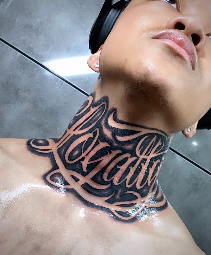 Man's neck with a large black ink script tattoo reading Loyalty in cursive.