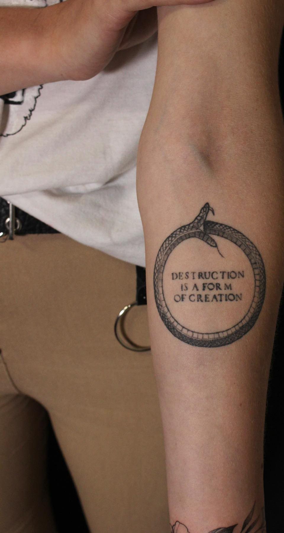 Snake ouroboros tattoo on an arm with text inside the circular snake body.