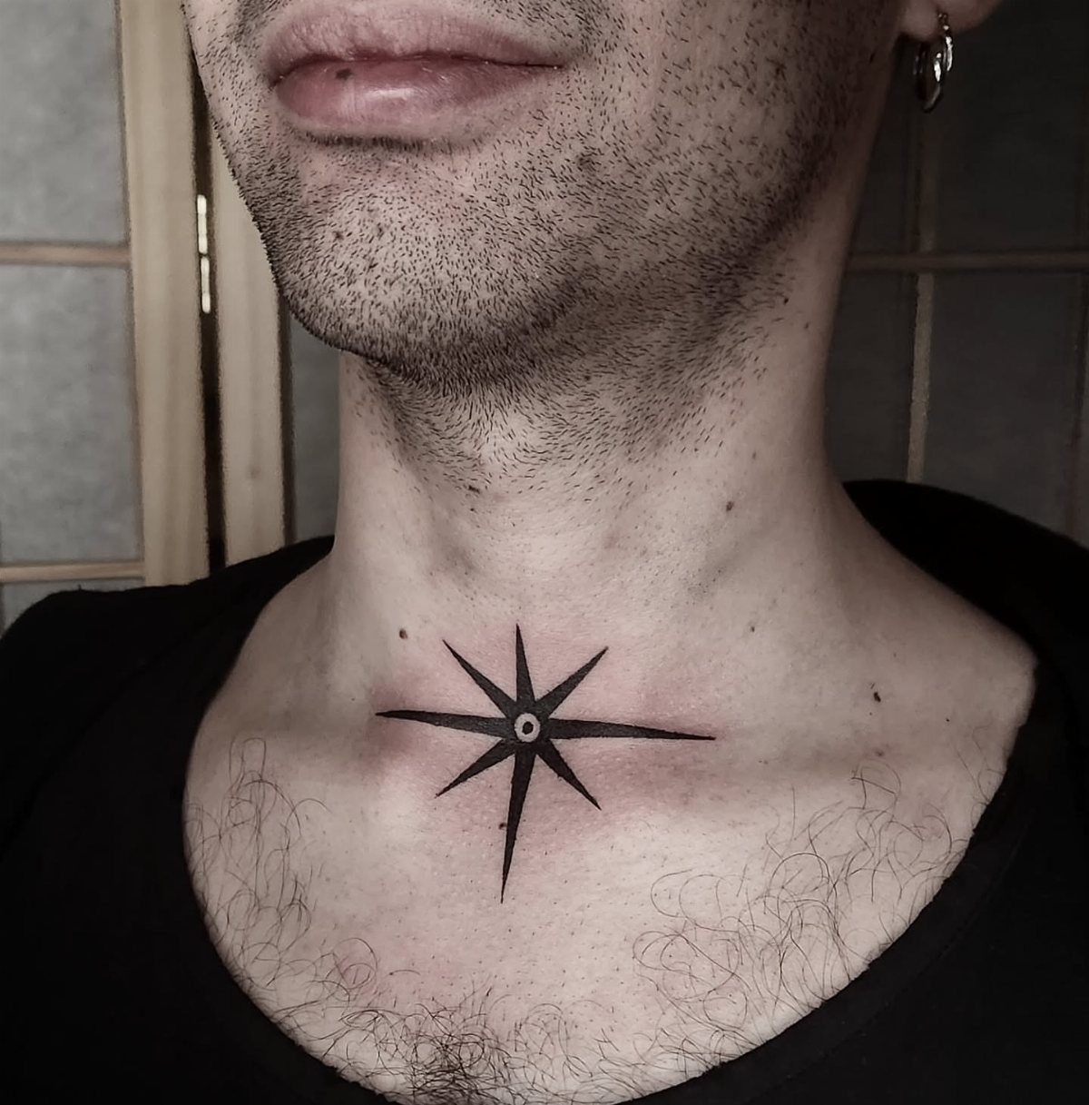 Black star tattoo on a man's neck and upper chest area.