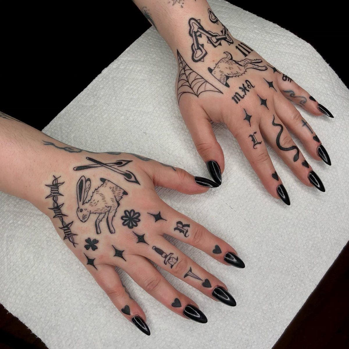Tattooed hands with black ink designs and long black nails on white towel