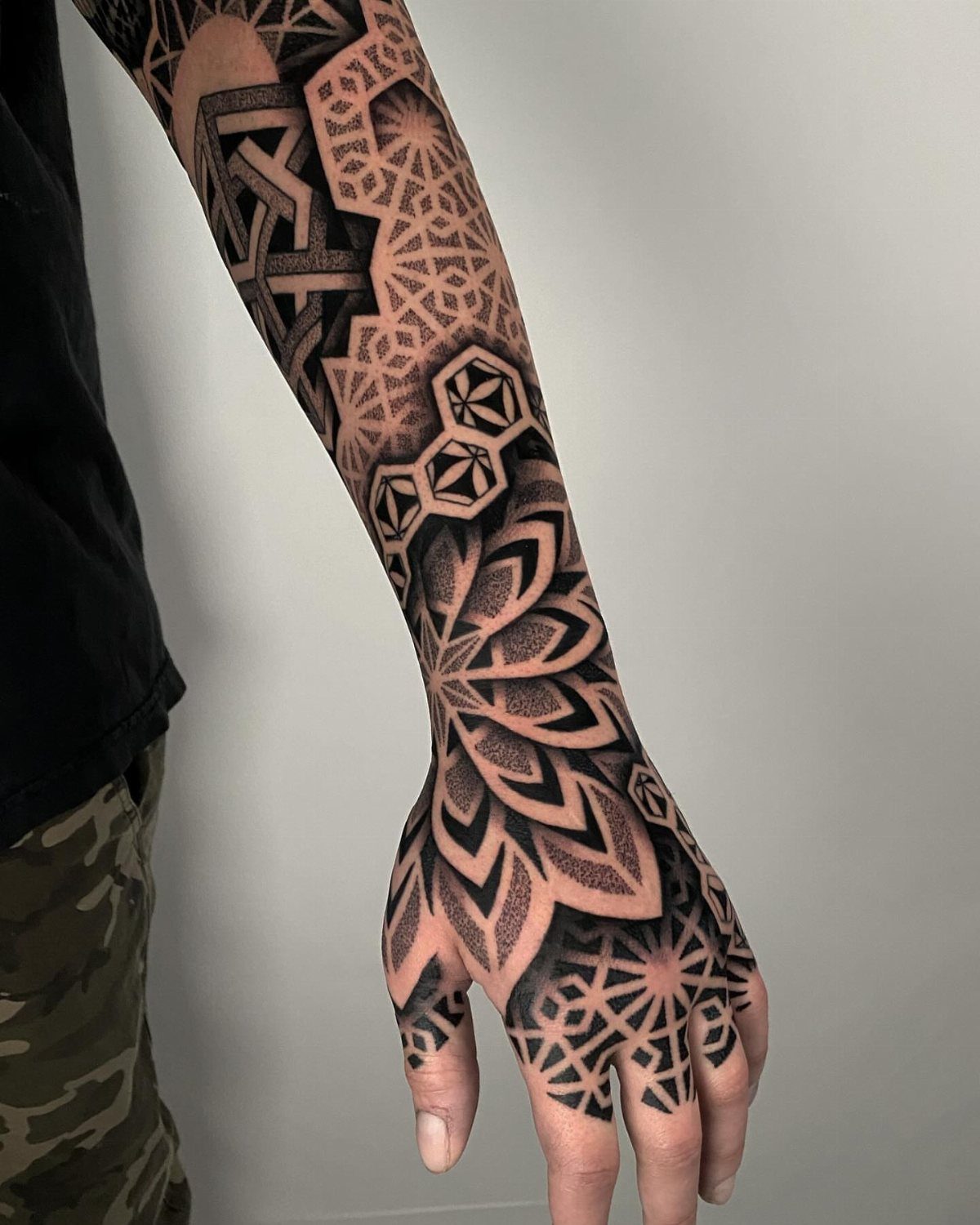 Geometric black and grey tattoo with symmetrical patterns covering a hand and forearm.