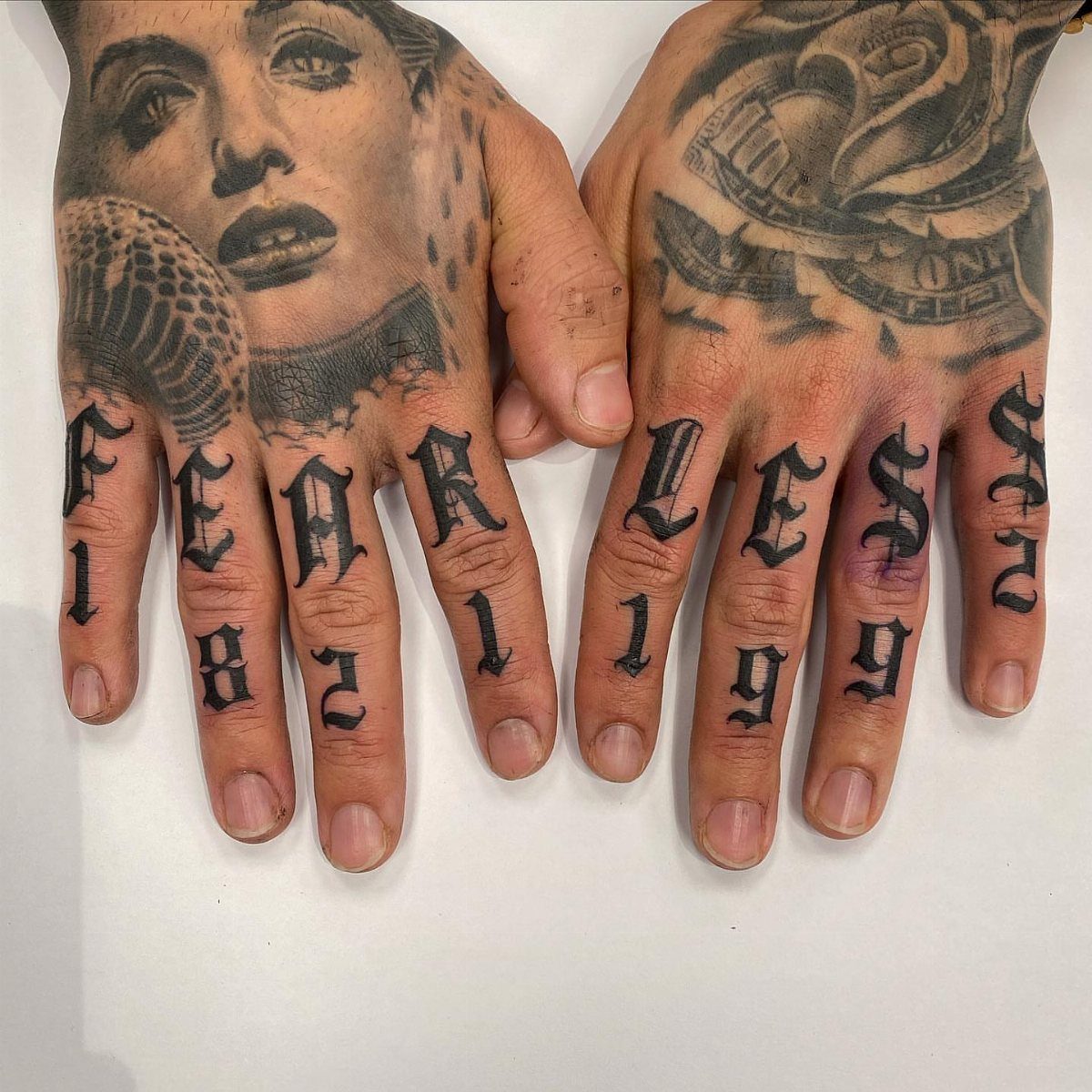 Tattooed hands featuring bold gothic lettering across the knuckles spelling out the word FEARLESS.