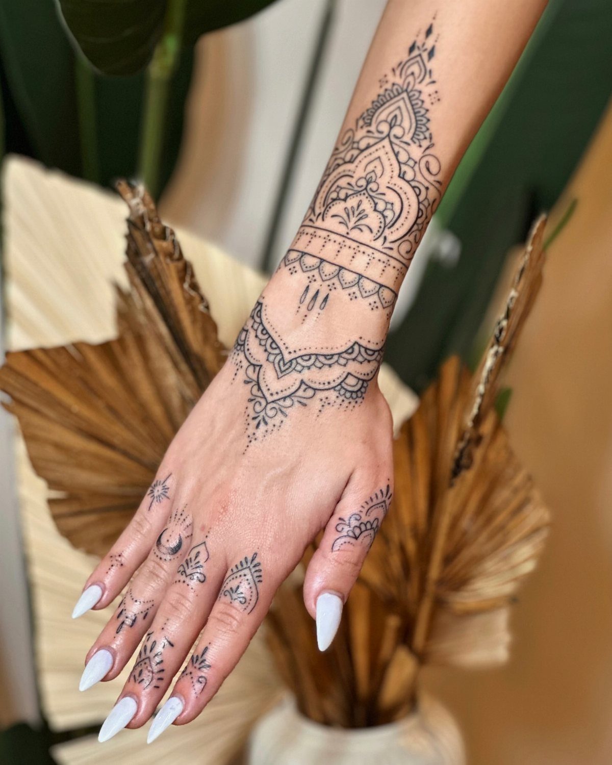 Hand and wrist with intricate black ornamental tattoos and long white nails.