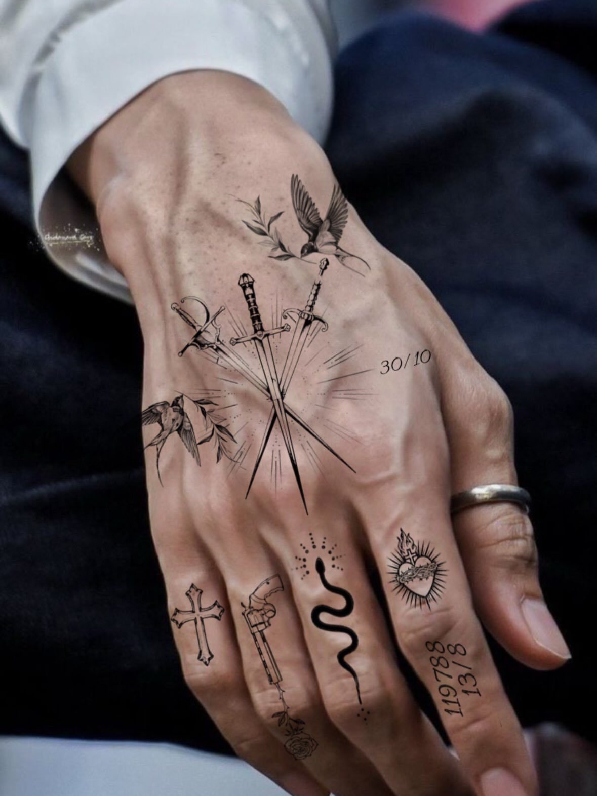Hand and fingers covered in various black ink tattoos including swords and symbols.