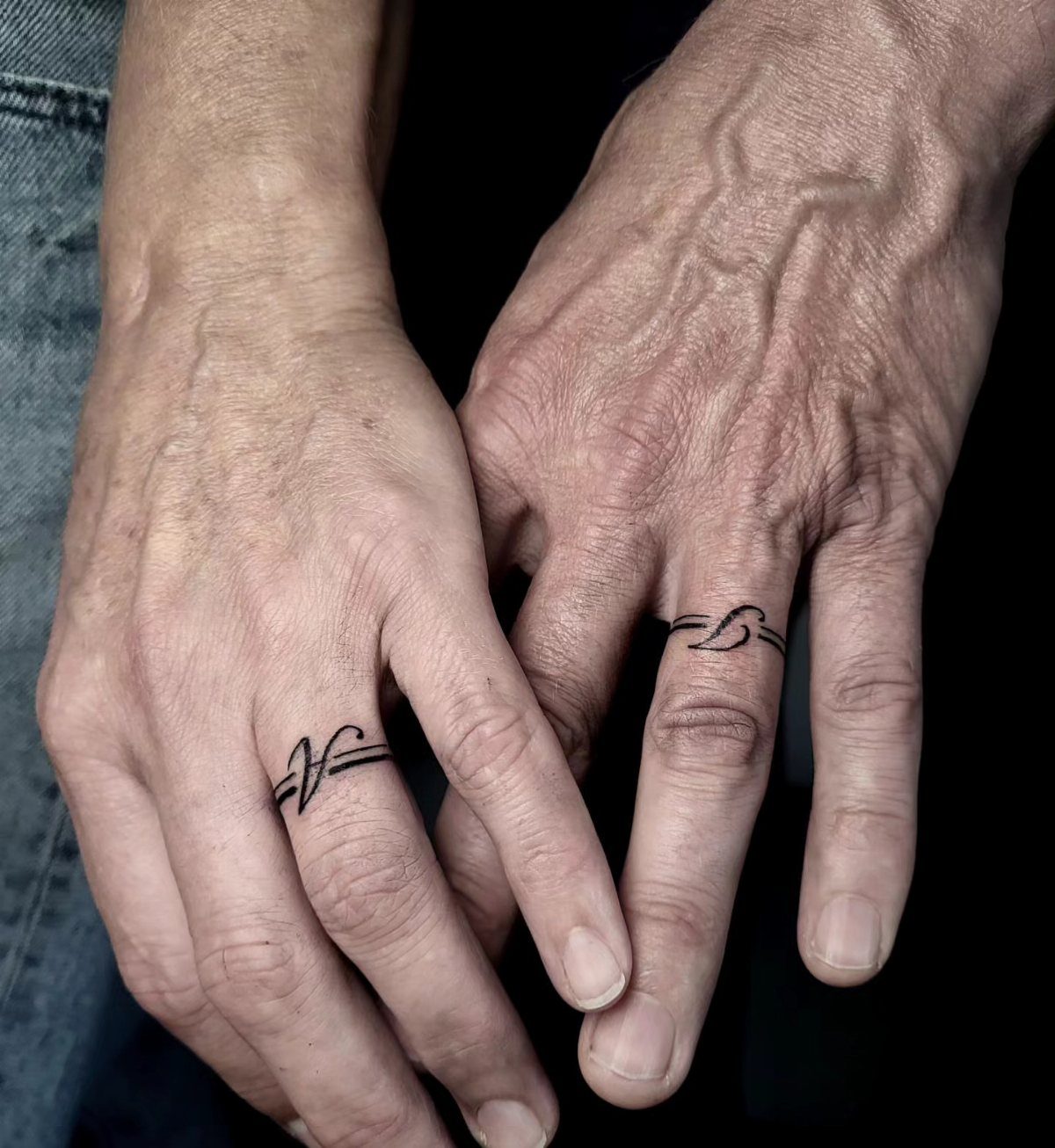 Two ring fingers with black ink band tattoos as wedding ring alternatives.