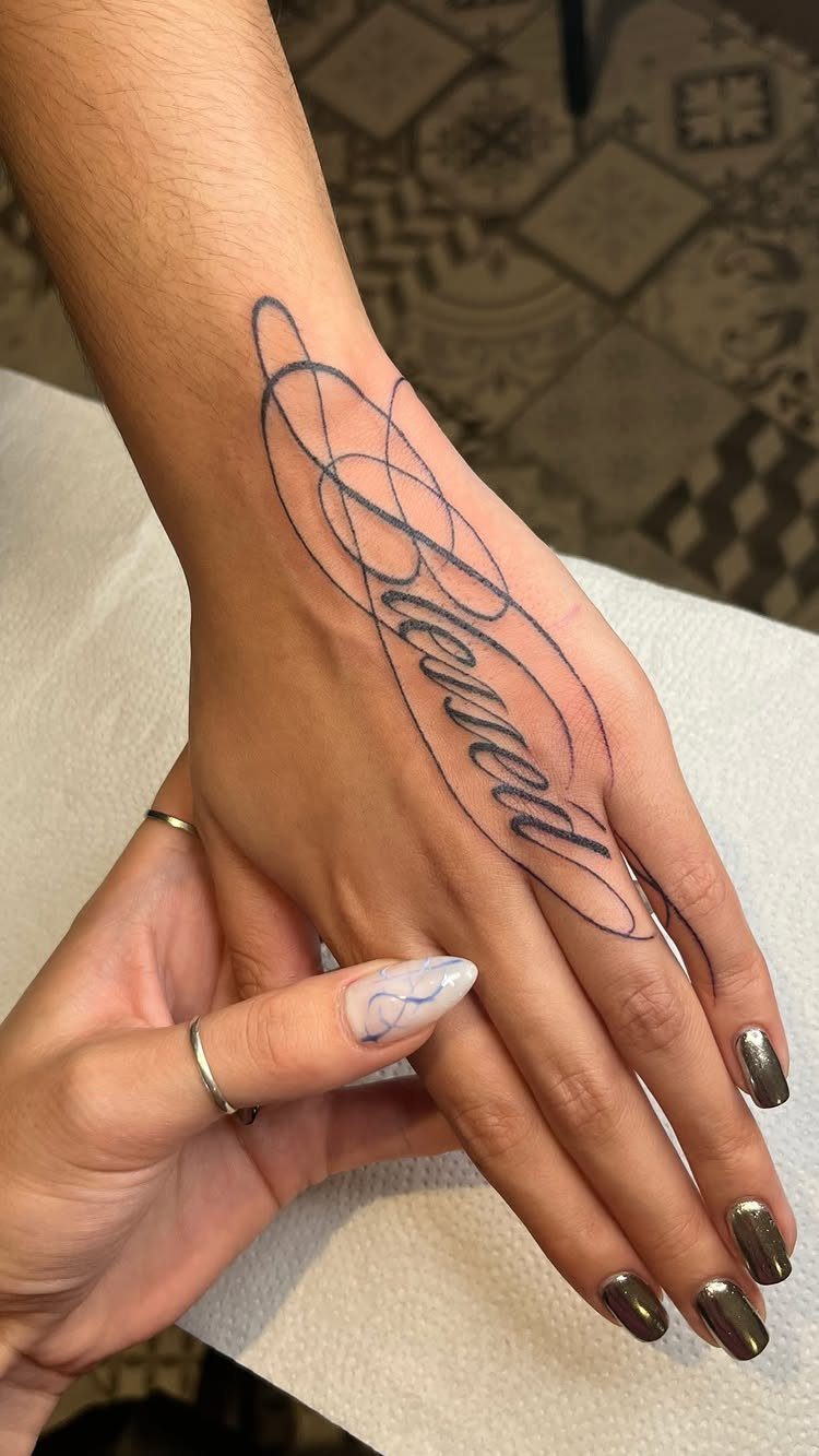 Cursive 'Blessed' tattoo with swirling lines on the back of a person's hand.