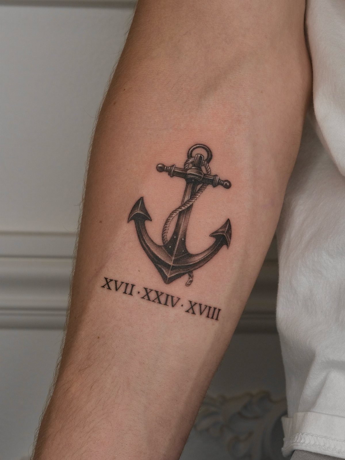 Nautical anchor tattoo with rope and Roman numerals on a man's forearm.