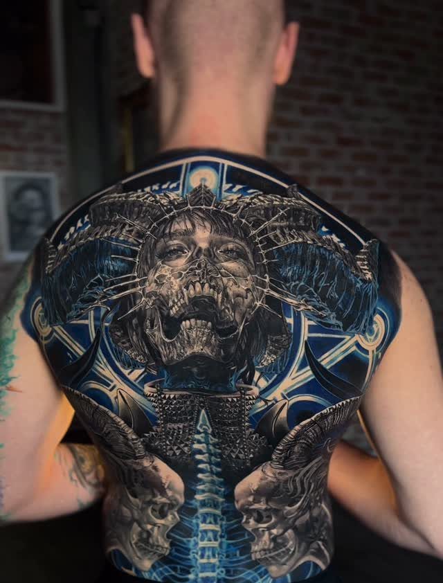Intricate back tattoo featuring a large central skull and biomechanical blue patterns.