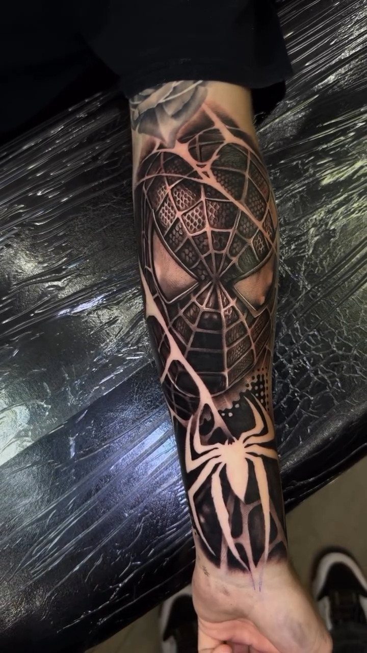Spider-Man mask and spider symbol blackwork tattoo on a man's forearm.