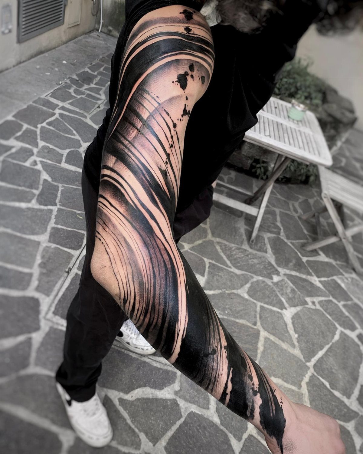 Leg tattoo with bold black brush stroke patterns and artistic ink splatters.