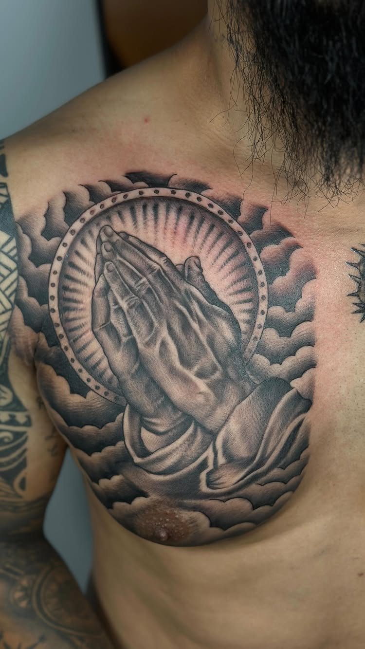 Praying hands tattoo with a halo and clouds on a man's chest