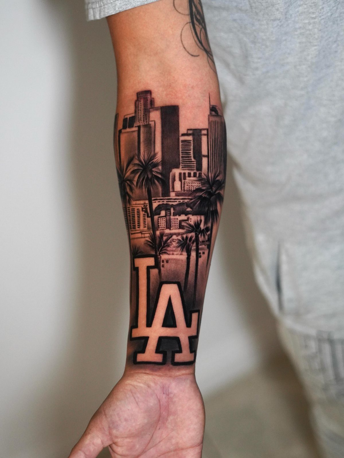 Cityscape tattoo on a forearm featuring Los Angeles buildings, palm trees, and LA lettering.