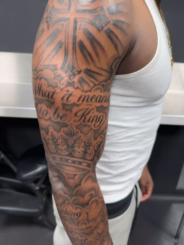 Tattoo on a man's arm featuring a crown, a cross, and script text.