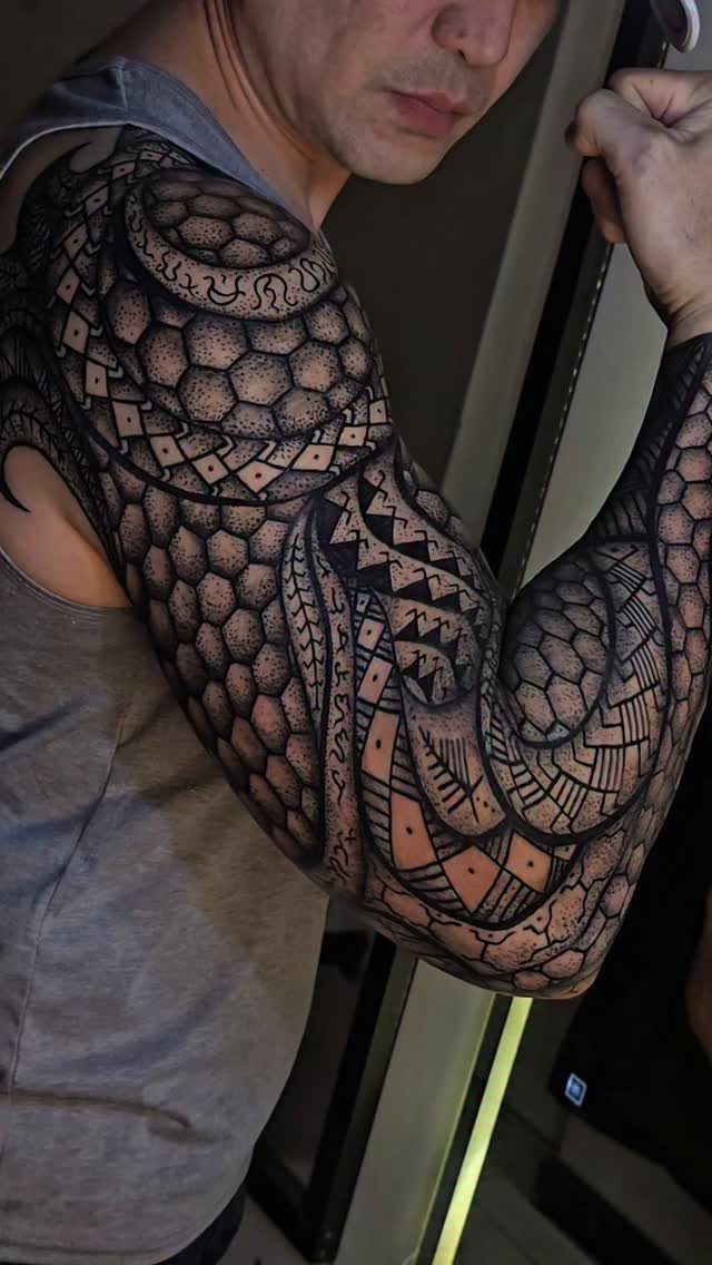 Full sleeve tattoo on a man's arm with black geometric and tribal patterns.