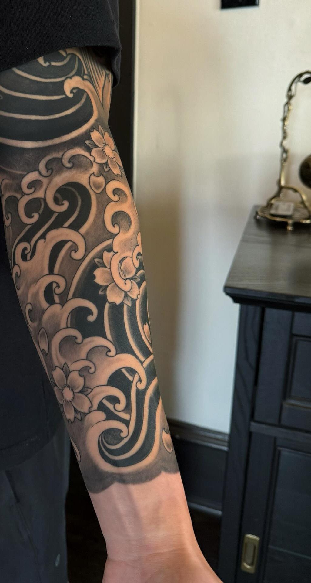 Ocean wave and flower tattoo on a man's arm in black and grey ink.