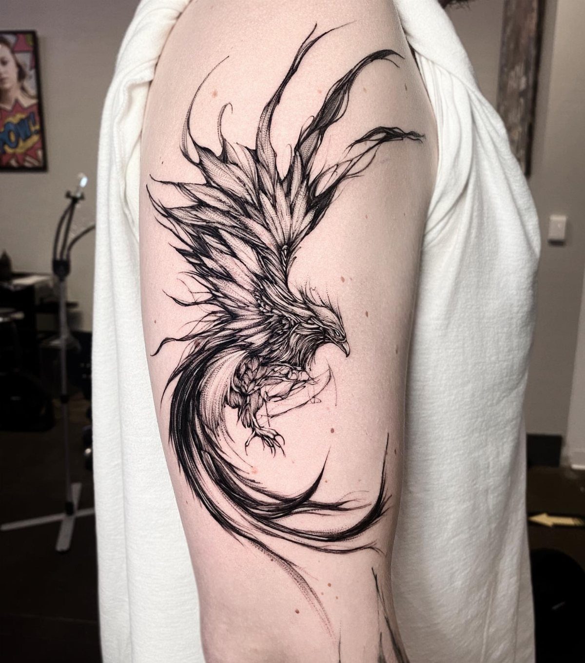 Phoenix tattoo with flowing black ink feathers on a man's upper arm.