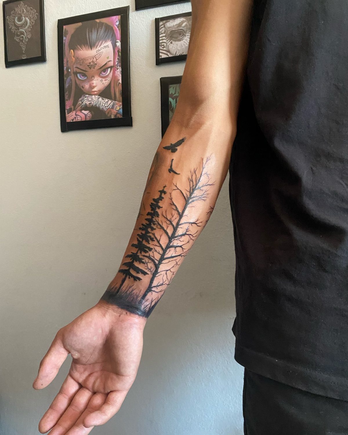 Forearm tattoo of black pine trees and birds on a man's arm.