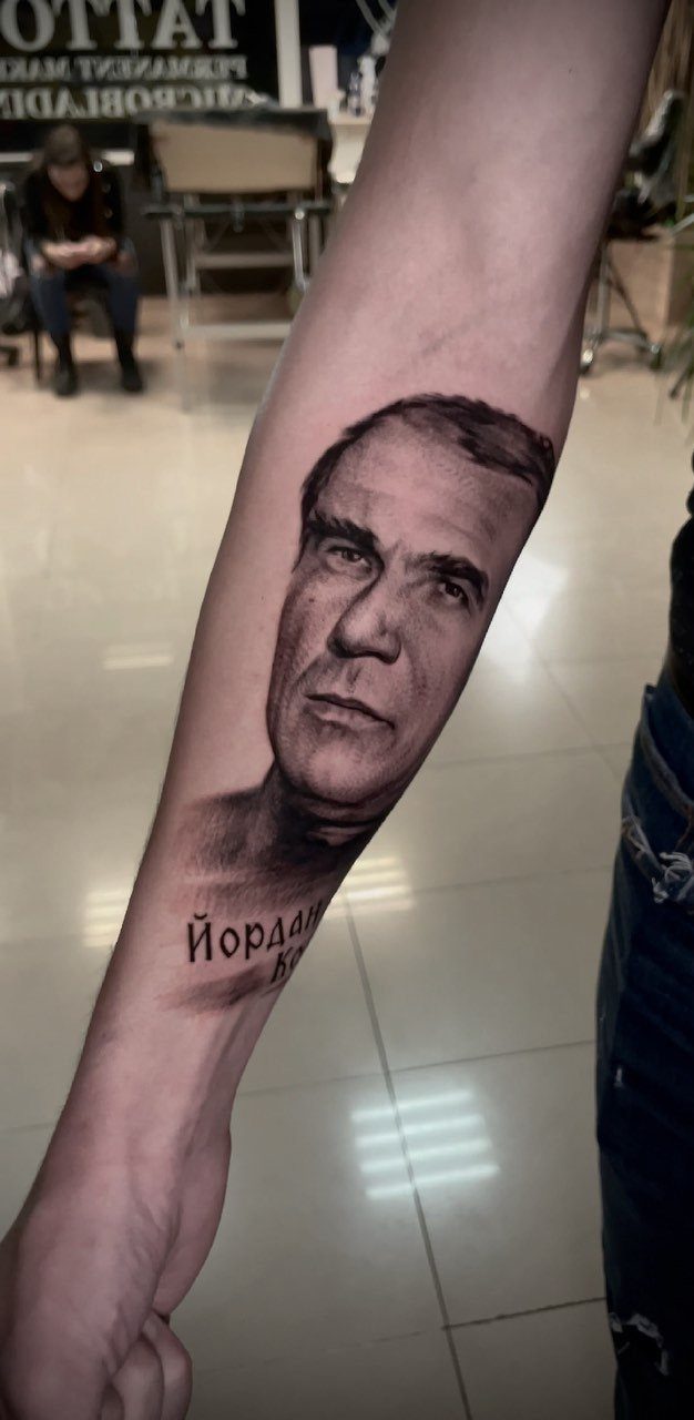 Realistic portrait tattoo of a man's face on a person's forearm.