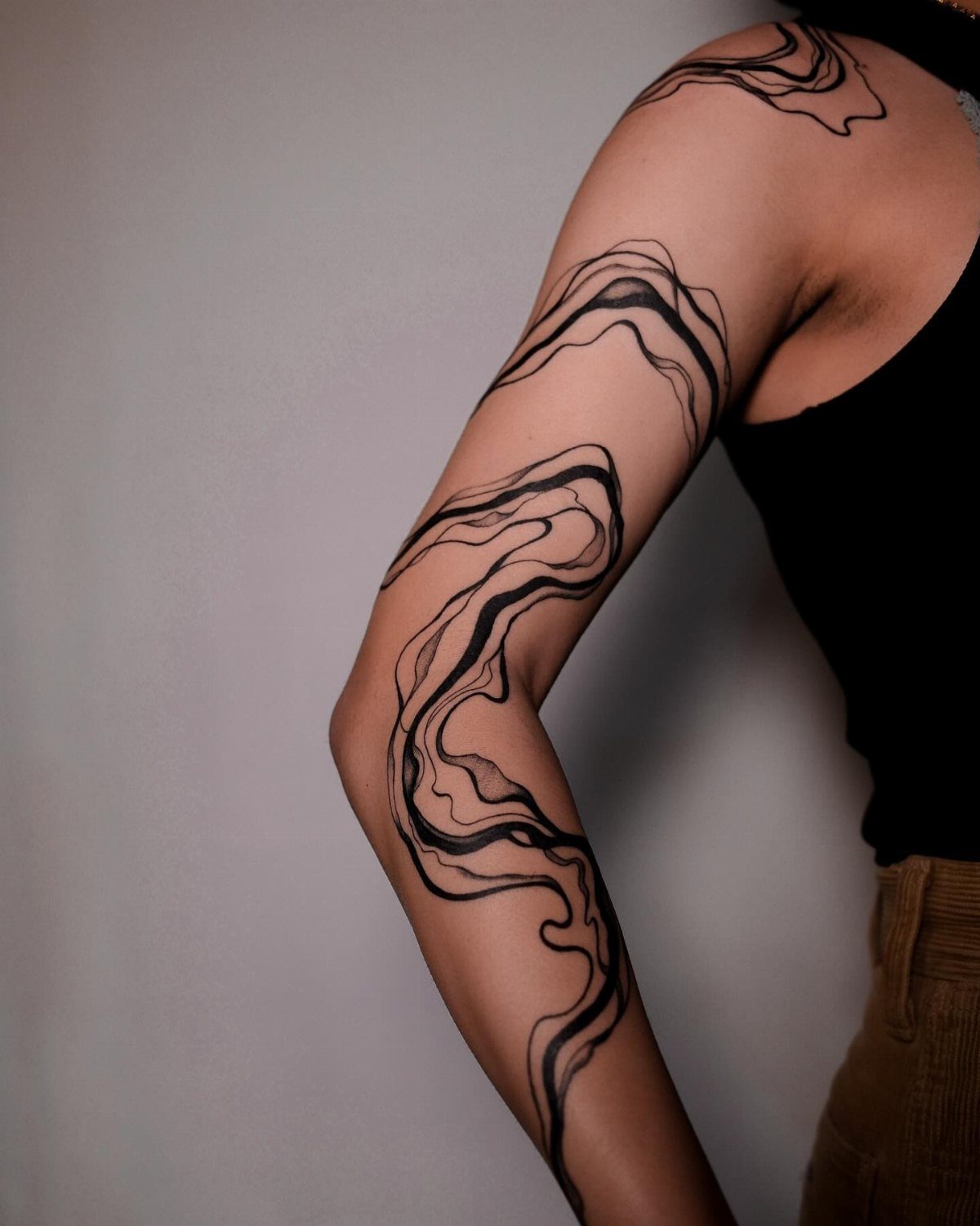 Abstract black ink tattoo of flowing organic lines on a person's shoulder and arm.