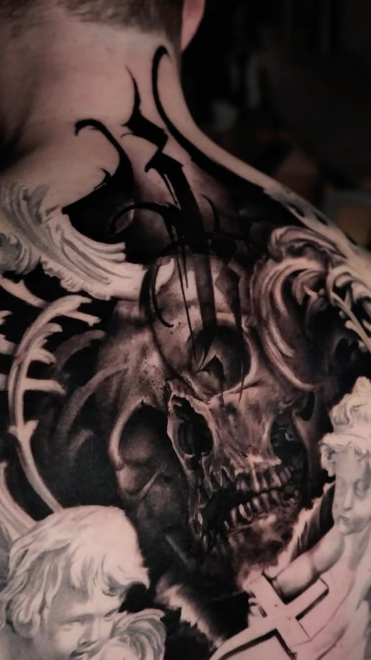 Baroque skull tattoo with ornamental filigree and cherubs on a person's shoulder
