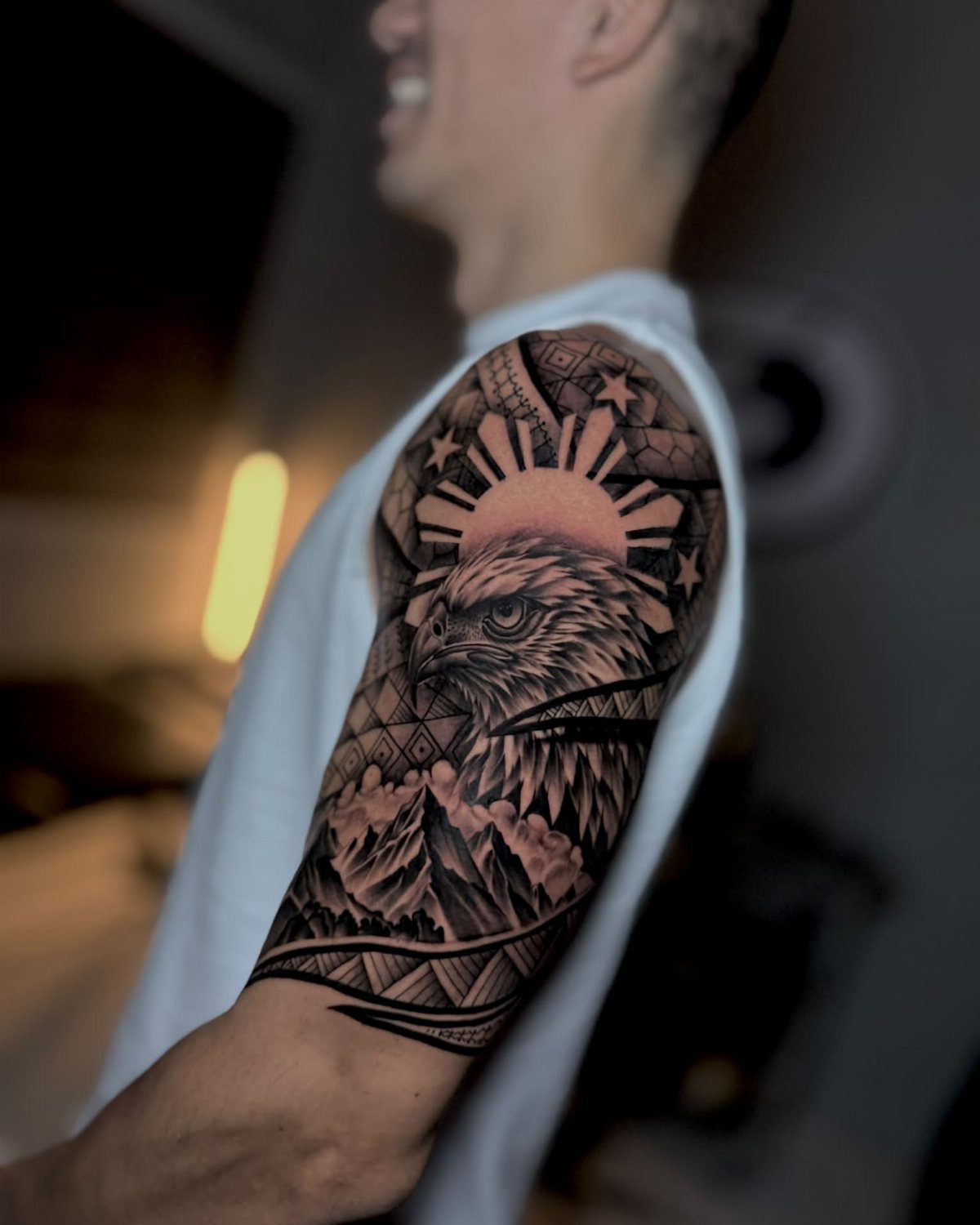 Eagle and sun tattoo on a man's shoulder with mountains and geometric patterns.