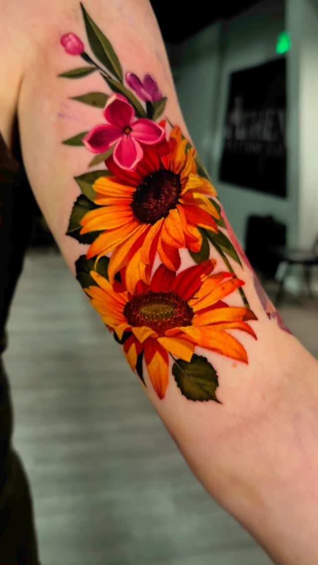 Floral shoulder tattoo featuring vibrant orange sunflowers and pink flowers on skin.