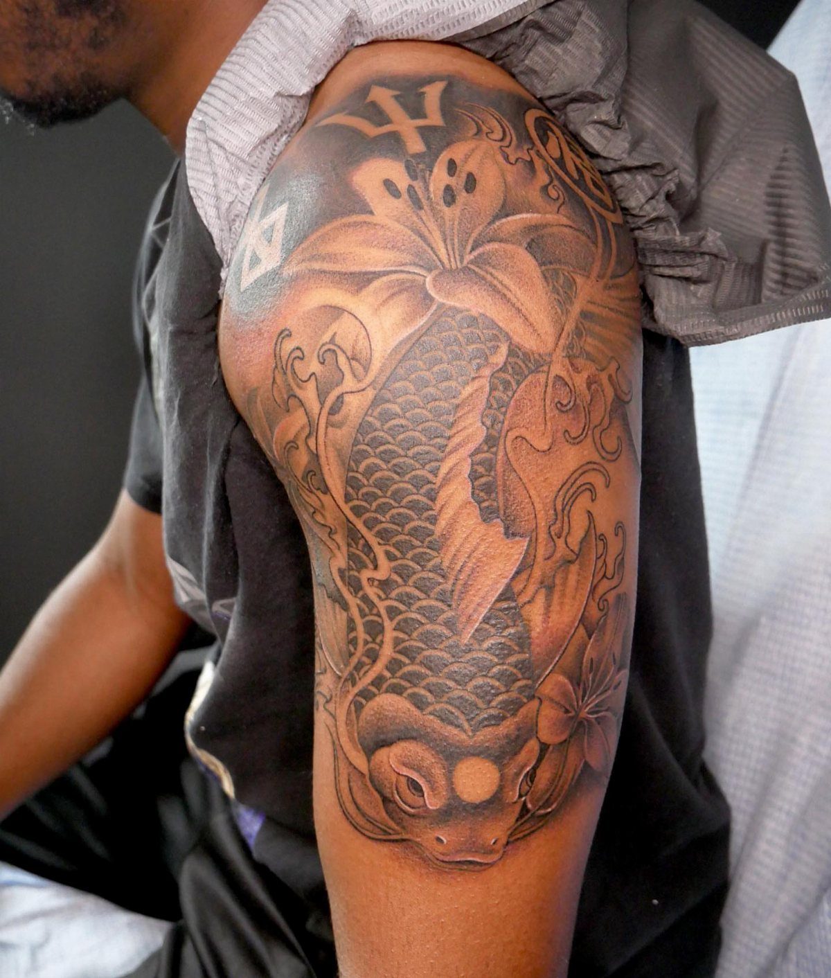 Koi fish tattoo swimming upwards with waves and lily on a shoulder