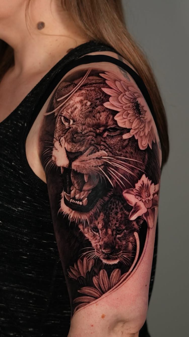 Lioness tattoo on a shoulder featuring a roaring lioness and flowers in black and grey.