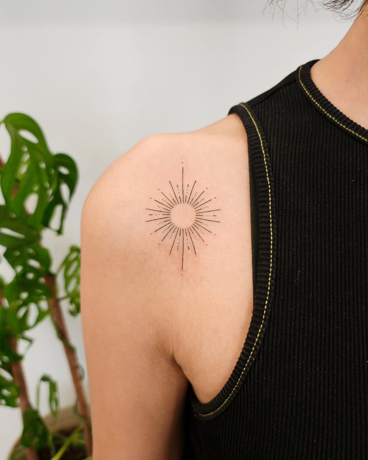 Minimalist sun tattoo with radiating lines on a person's shoulder