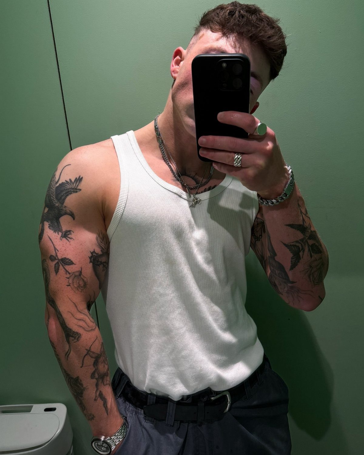Man with patchwork tattoos on his shoulder and arm taking a mirror selfie.