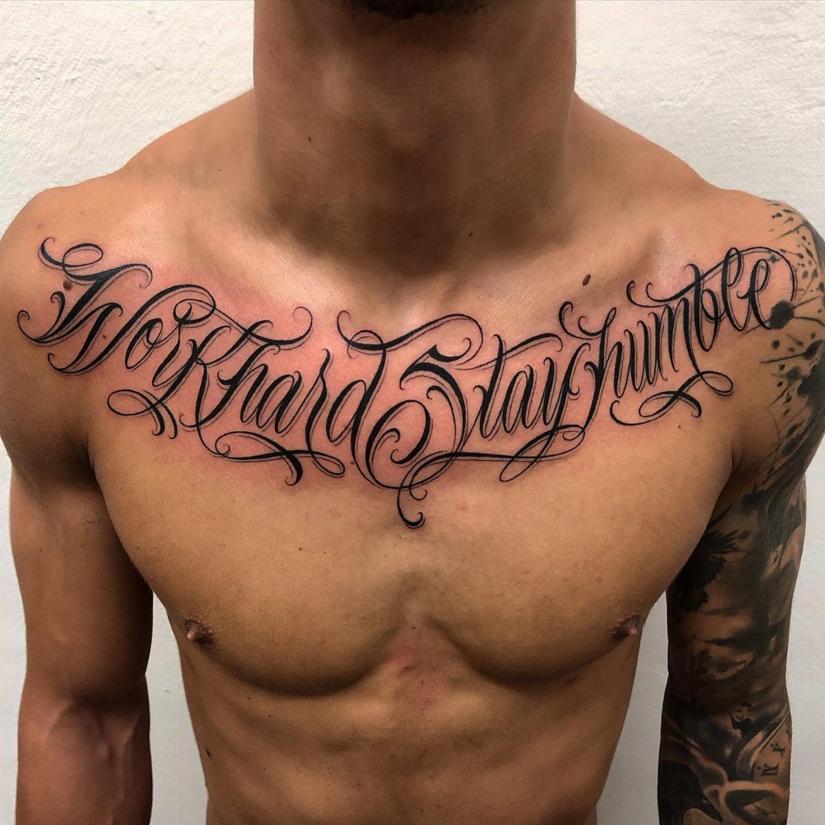 Cursive black ink tattoo on a man's chest reading Work Hard Stay Humble