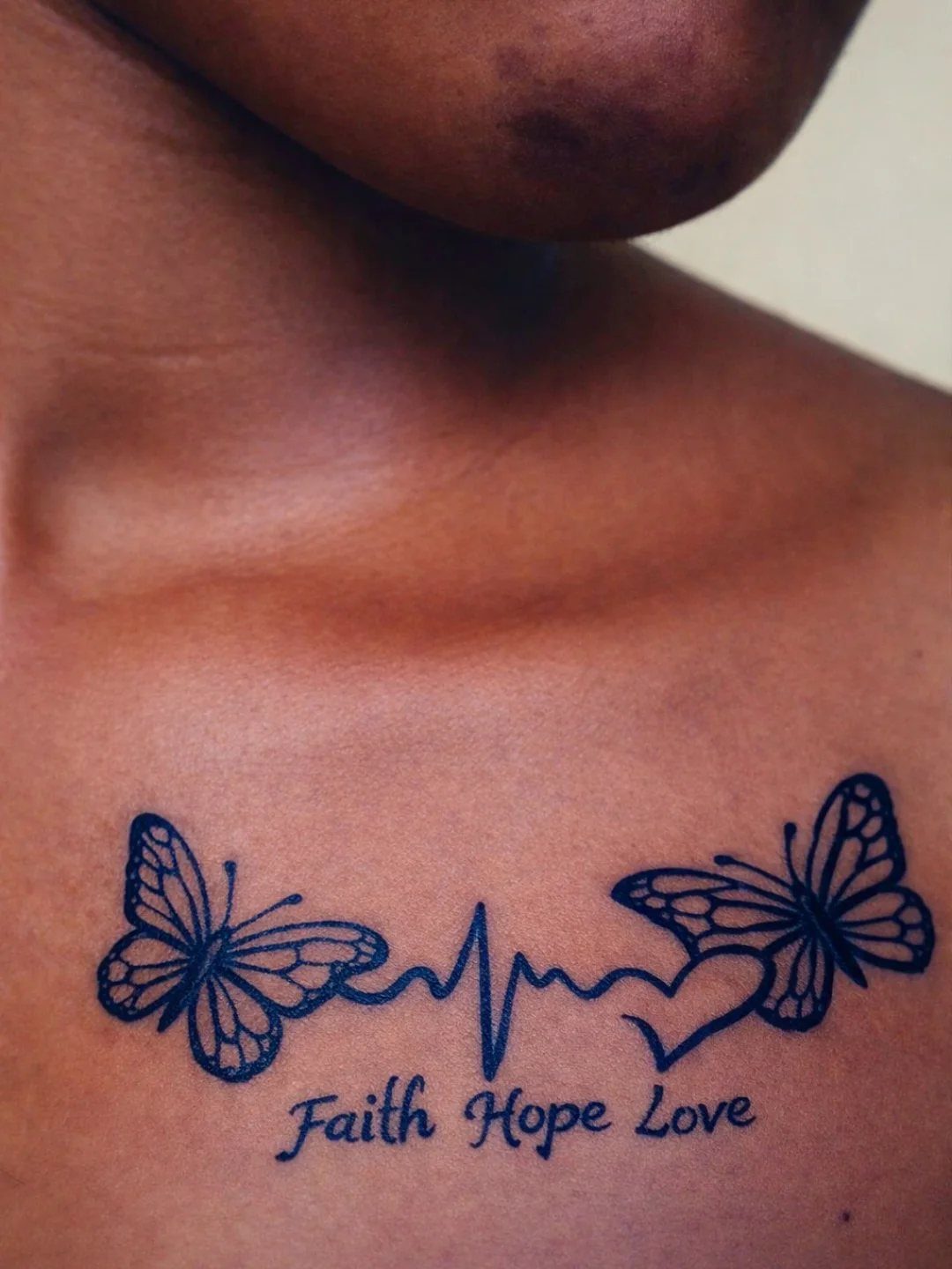 Chest tattoo featuring butterflies, a heartbeat line, a heart, and the words Faith Hope Love