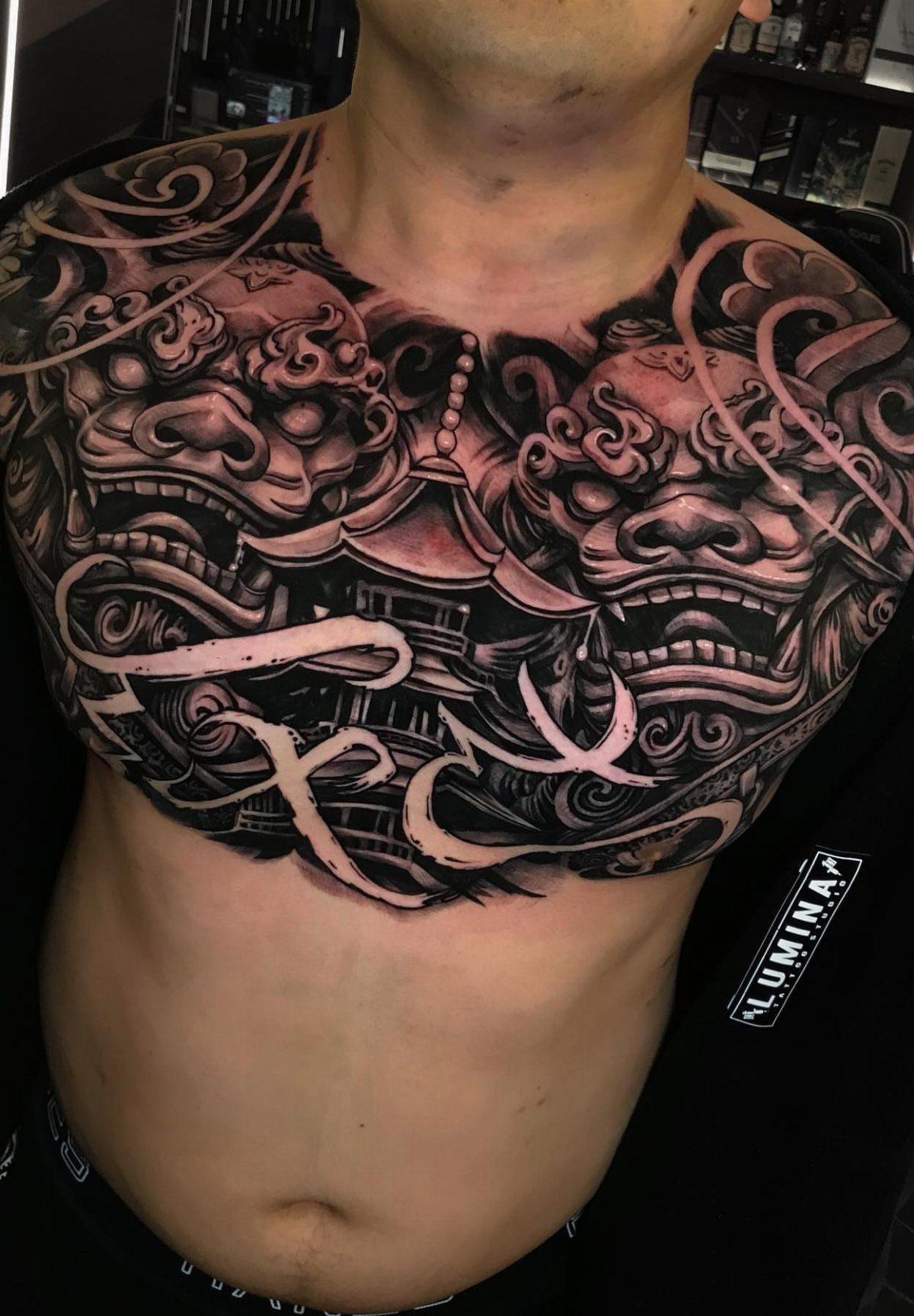 Detailed black and grey Japanese style chest tattoo featuring lion dogs and a pagoda.