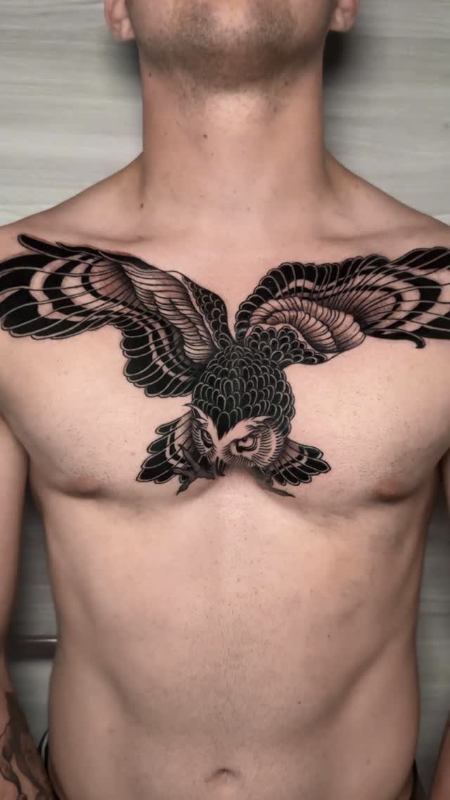 Owl tattoo with spread wings across a man's chest in black ink.