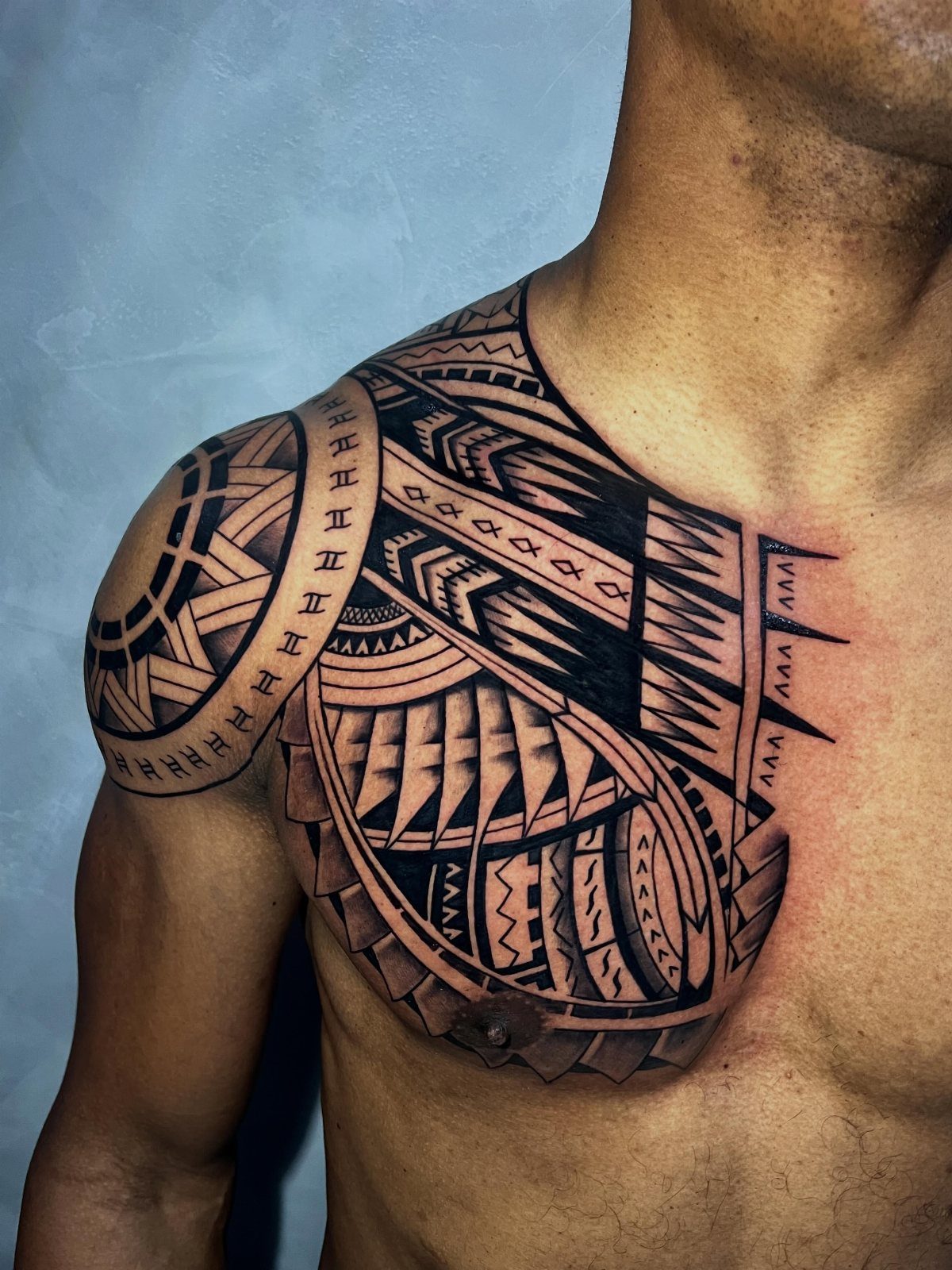 Polynesian tribal tattoo covering a man's shoulder and upper chest area.