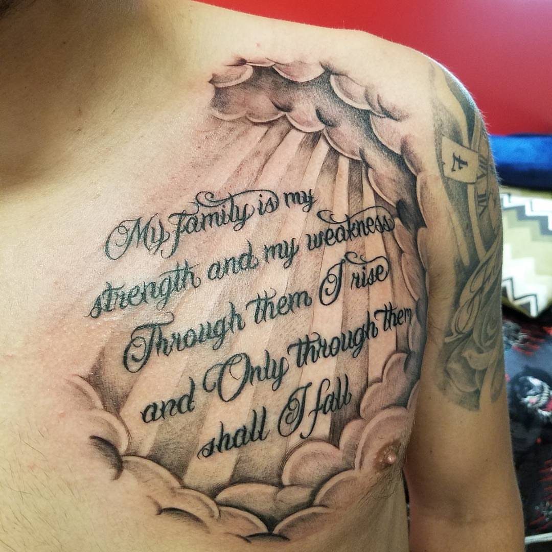 Chest tattoo with a cursive quote surrounded by clouds and light rays.