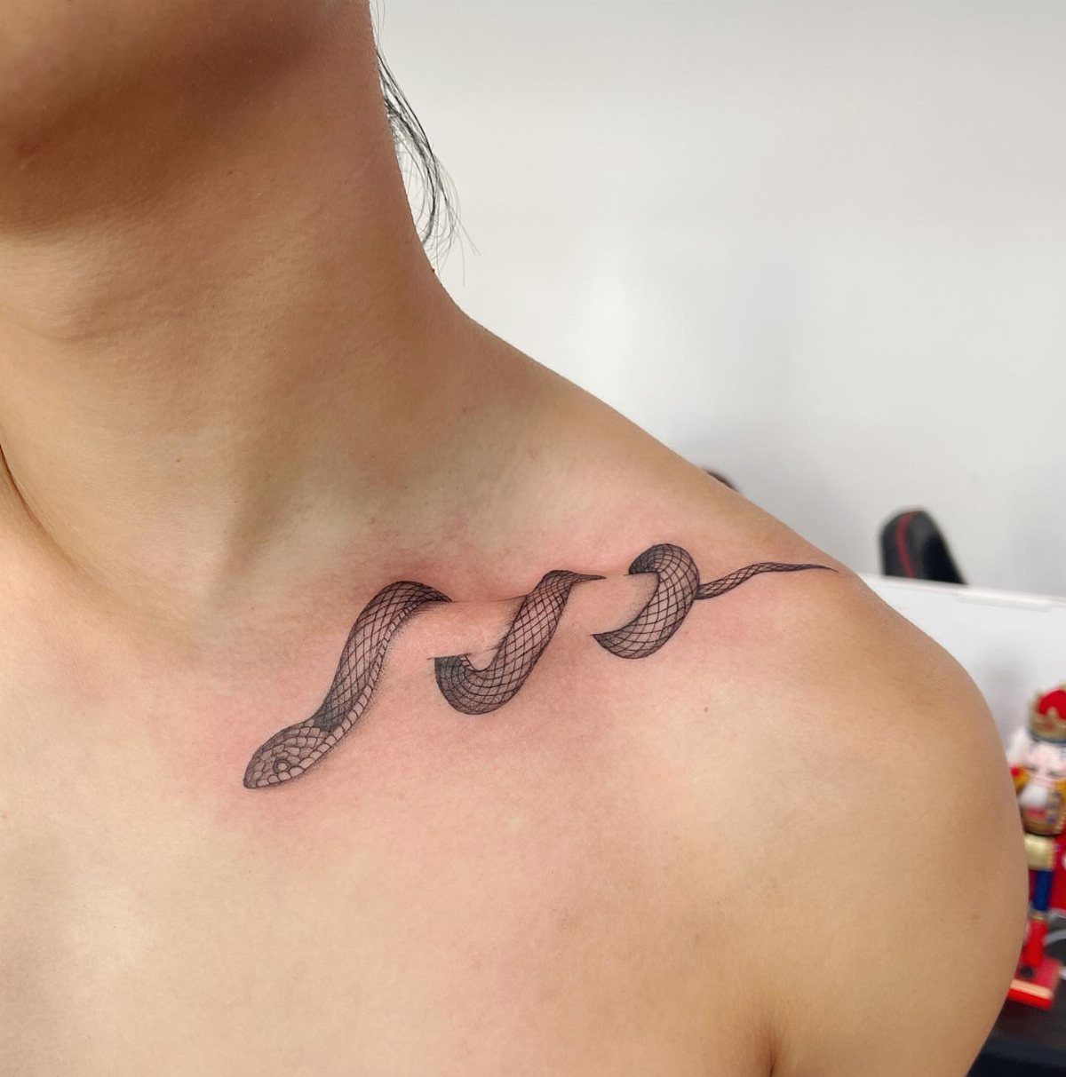 Three small black snake tattoos curving along a person's collarbone and upper chest.