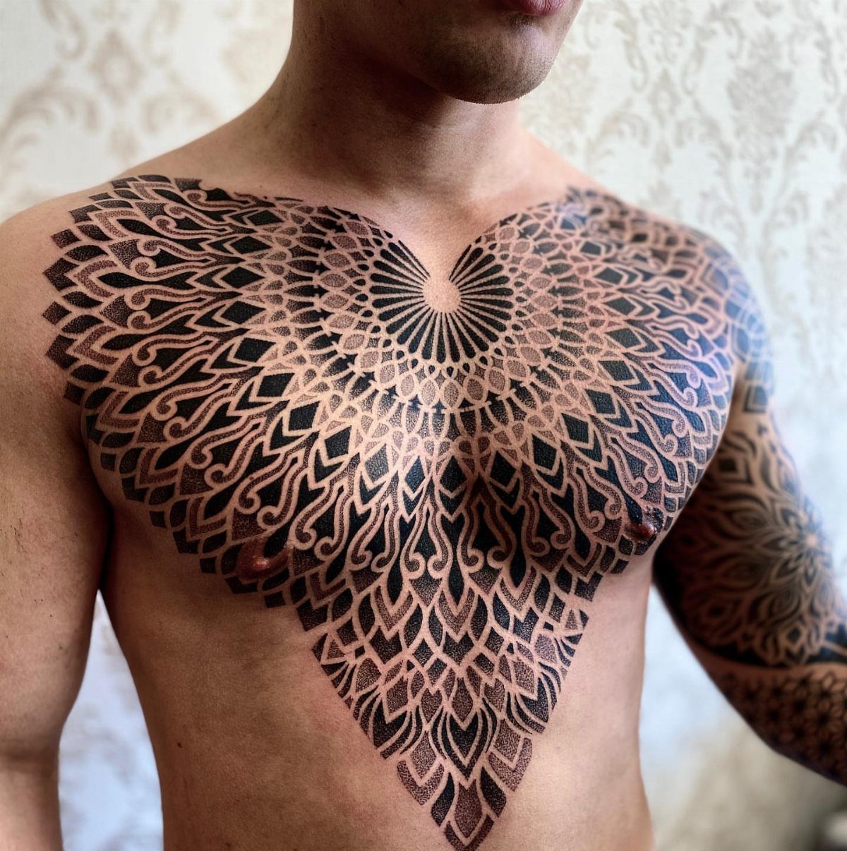 Intricate black ink mandala tattoo covering a man's chest and sternum area.