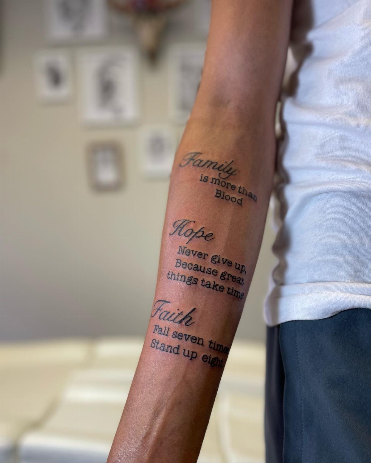 Forearm with three black ink text tattoos featuring family, hope, and faith quotes.