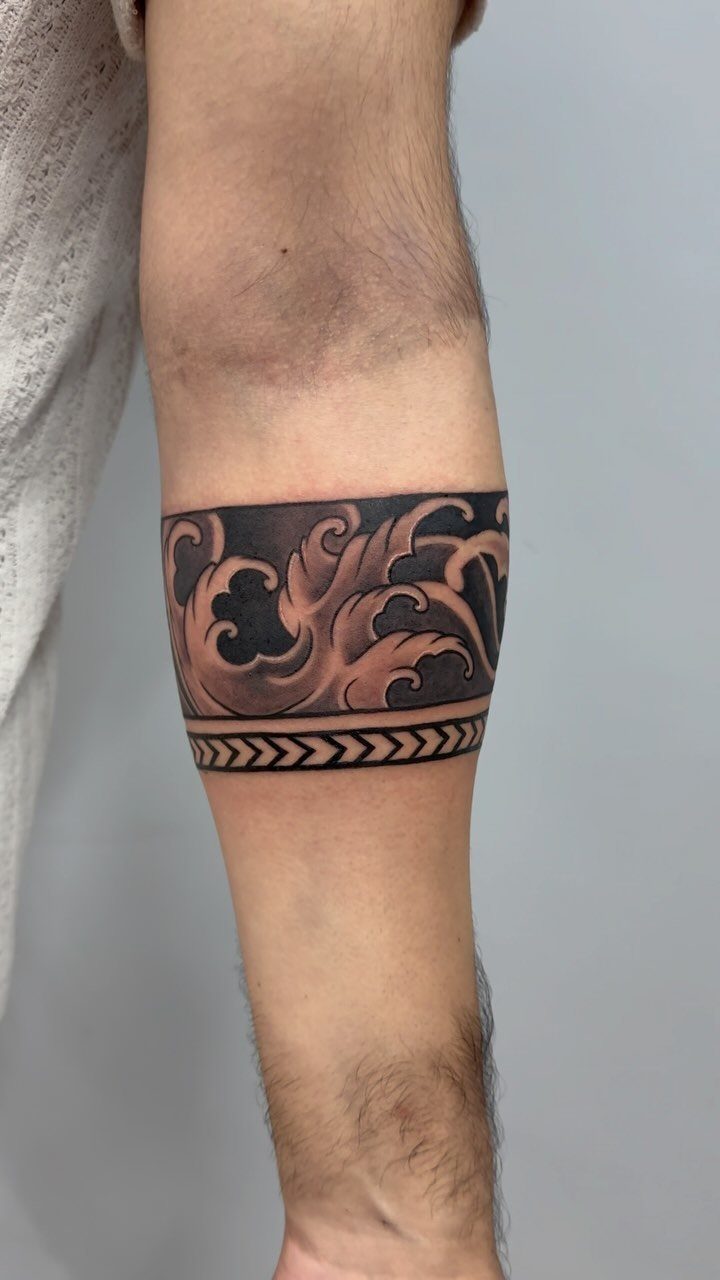 Armband tattoo with ornate scrolls and geometric patterns wrapping around a forearm.