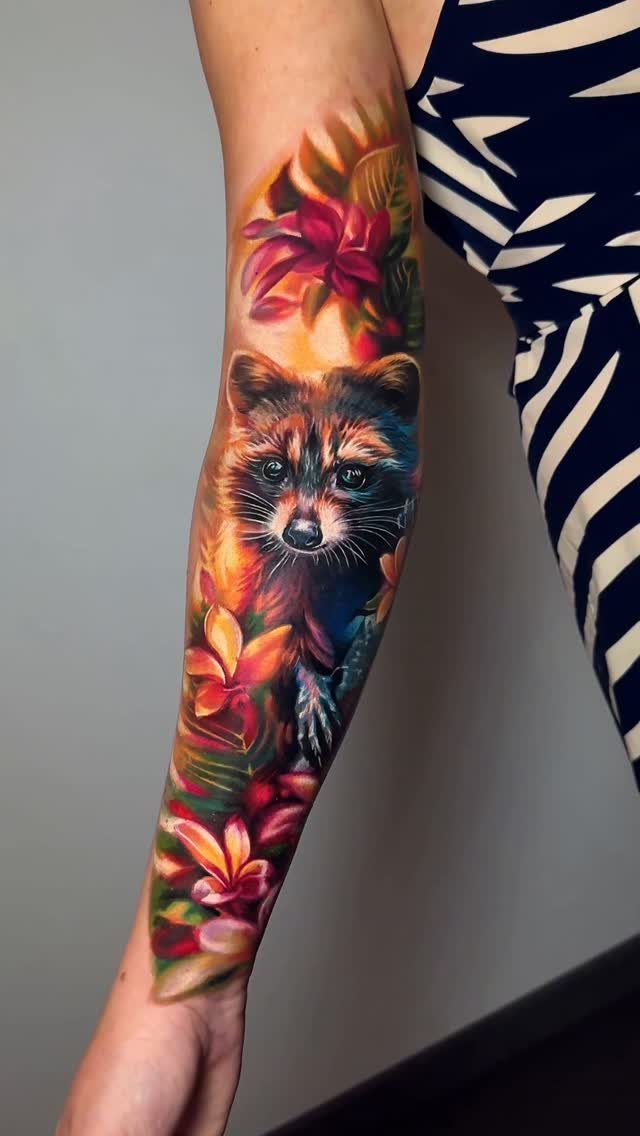 Raccoon tattoo with colorful tropical flowers on a person's forearm