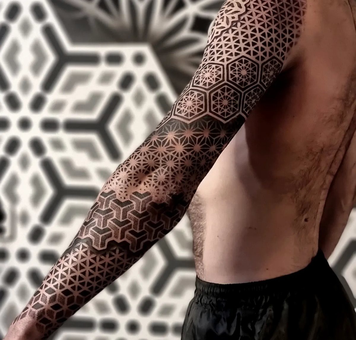 Geometric tattoo of interlocking hexagonal patterns covering a man's shoulder and arm.