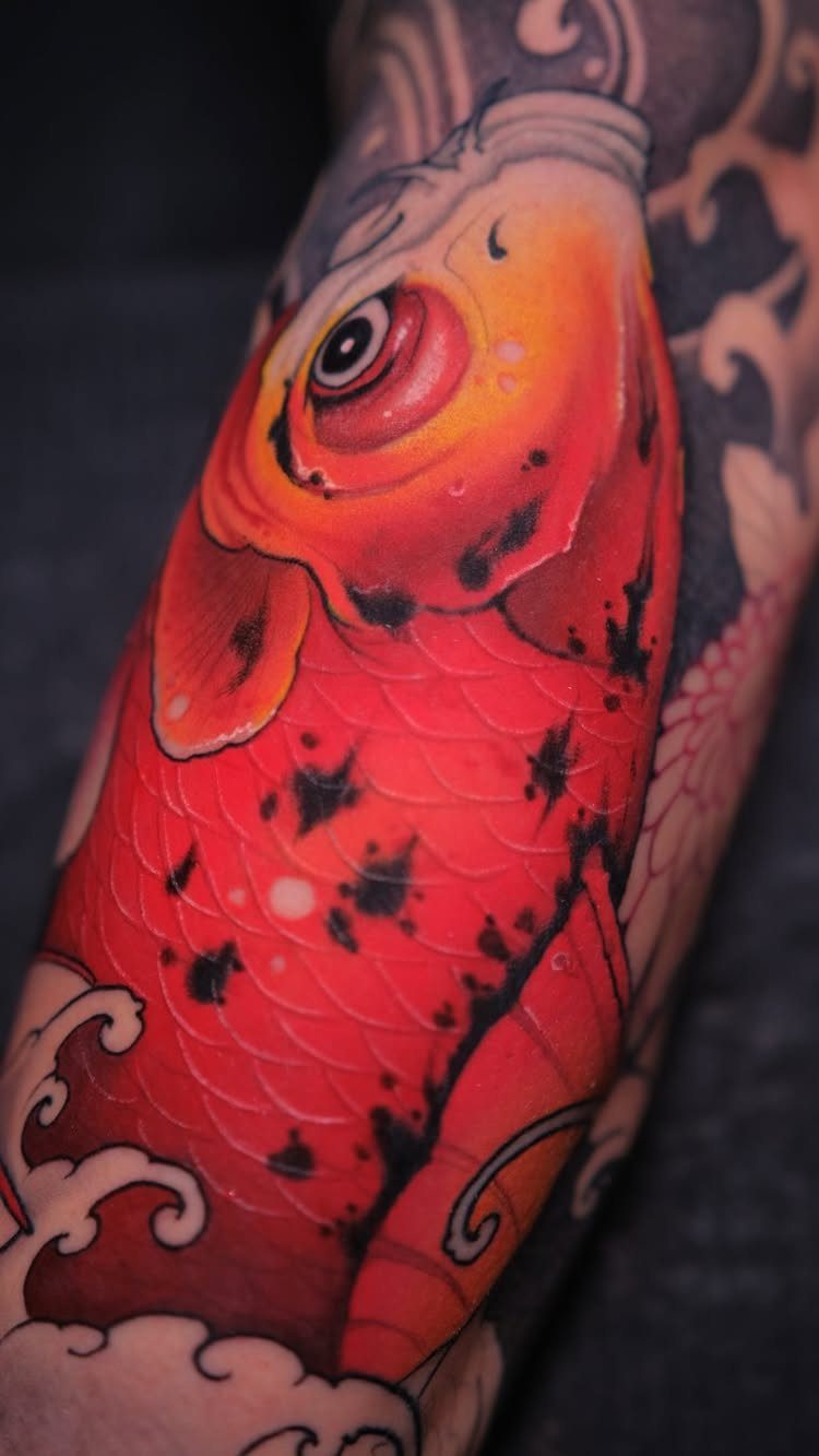 Red koi fish tattoo with black and grey waves on a person's arm